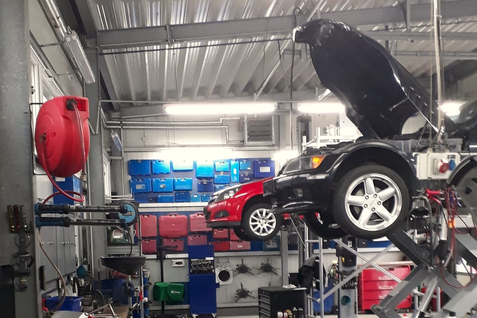 Fahrzeug mit geöffneter Motorhaube auf der Scherenbühne in der Werkstatthalle von Automobile Beckmann, dahinter die Teileregale