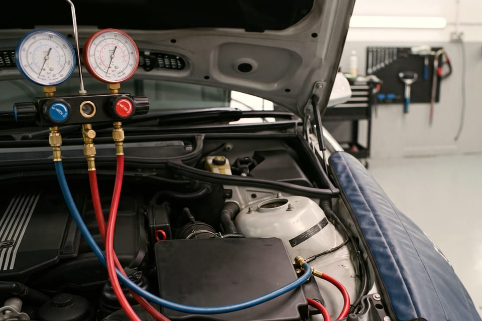 Manometerbrücke eines Klimaservicegeräts, roter und blauer Schlauch führen in den Motorraum, Kotflügelabdeckung aufgelegt