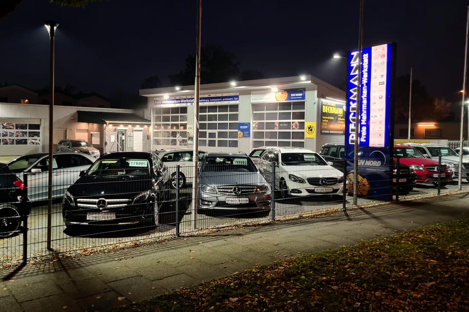 Der beleuchtete Verkaufshof von Automobile Beckmann am Abend, Fahrzeuge mit Preisschild in der Scheibe